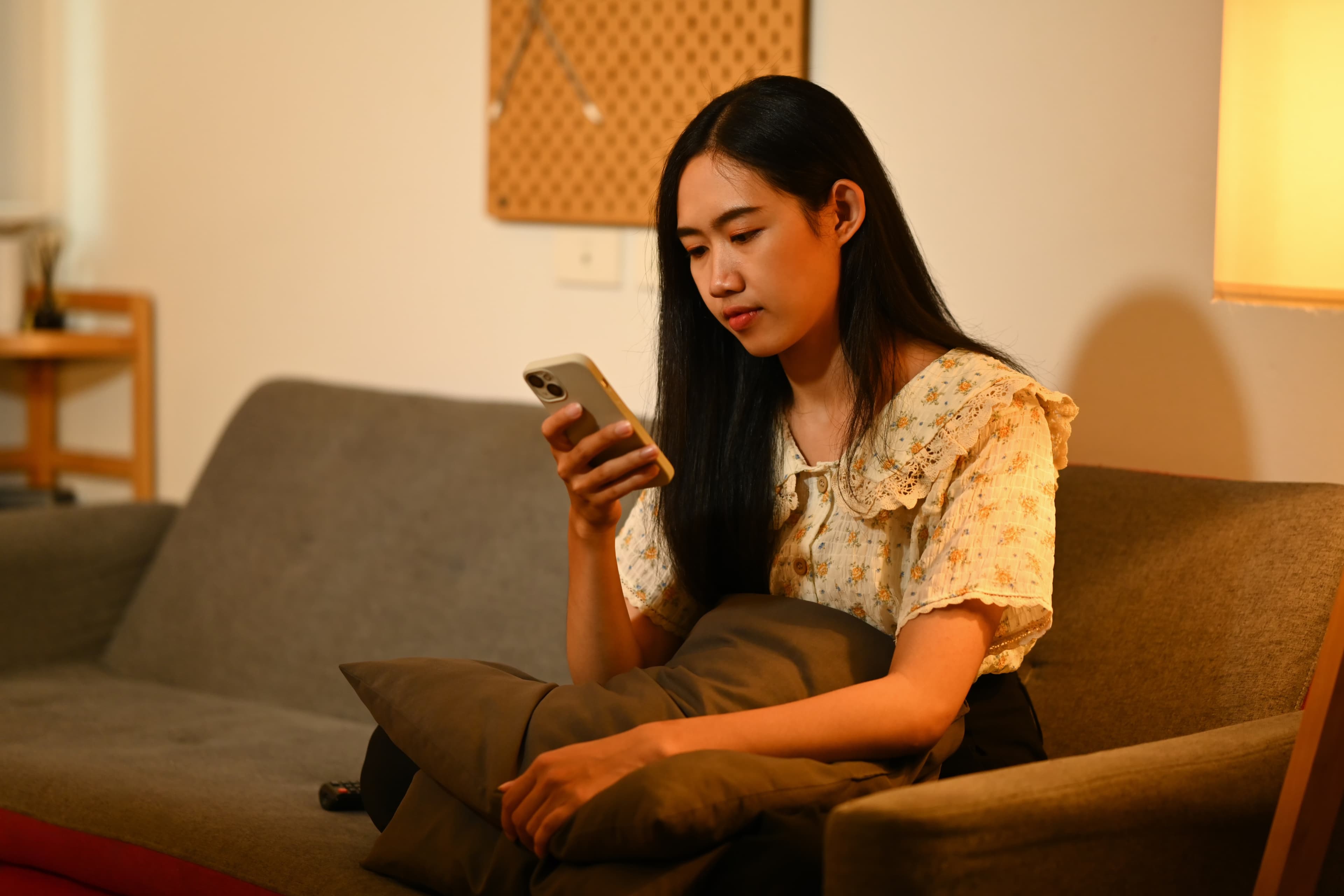 Woman checking her phone in a warmly lit living room.